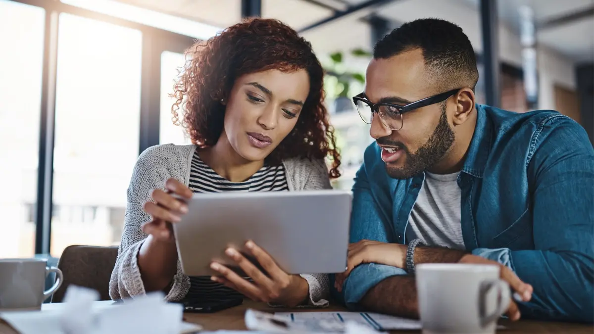Two people sitting in an office in front of a window looking at a notepad and discussing its content.